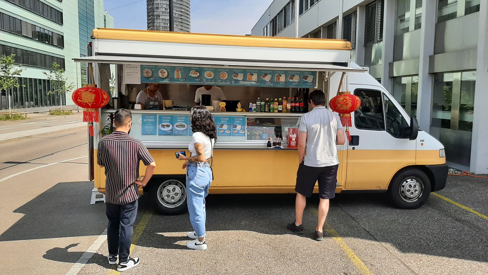 Drei Menschen warten vor einem Foodtruck auf ihr Essen.